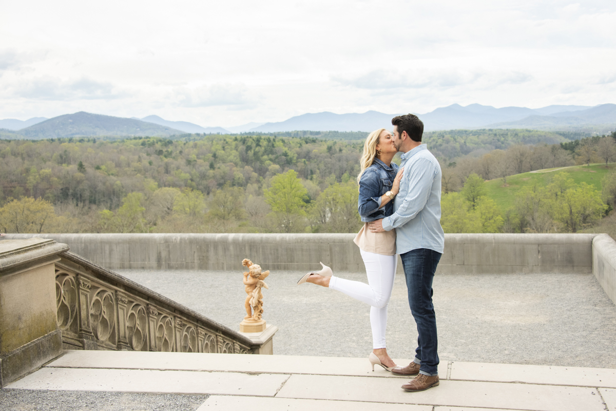 Engaged couple kissing at Biltmore Estate with mountain view.