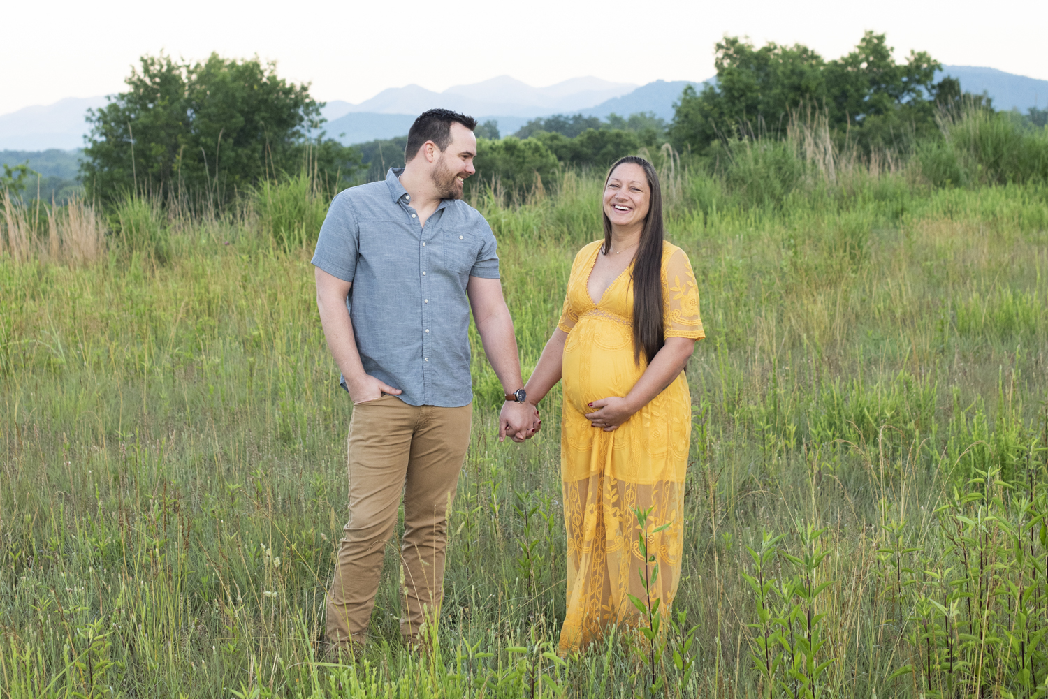 Couple holding hands and laughing during maternity photos with mountain views
