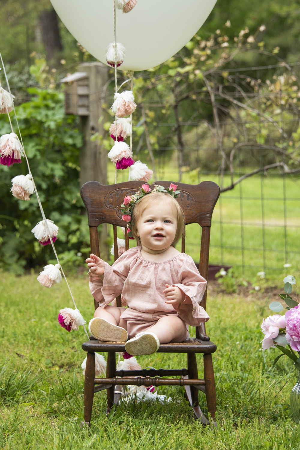 One year old girl during birthday photos sitting in chair with big balloons