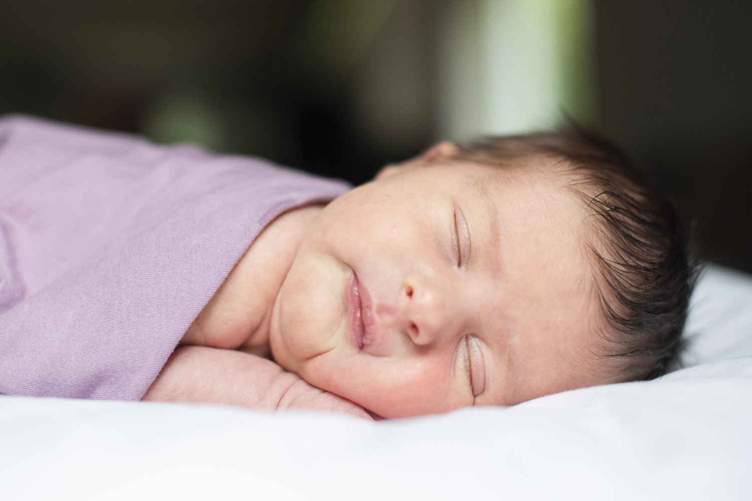 Baby girl on belly in purple swaddle