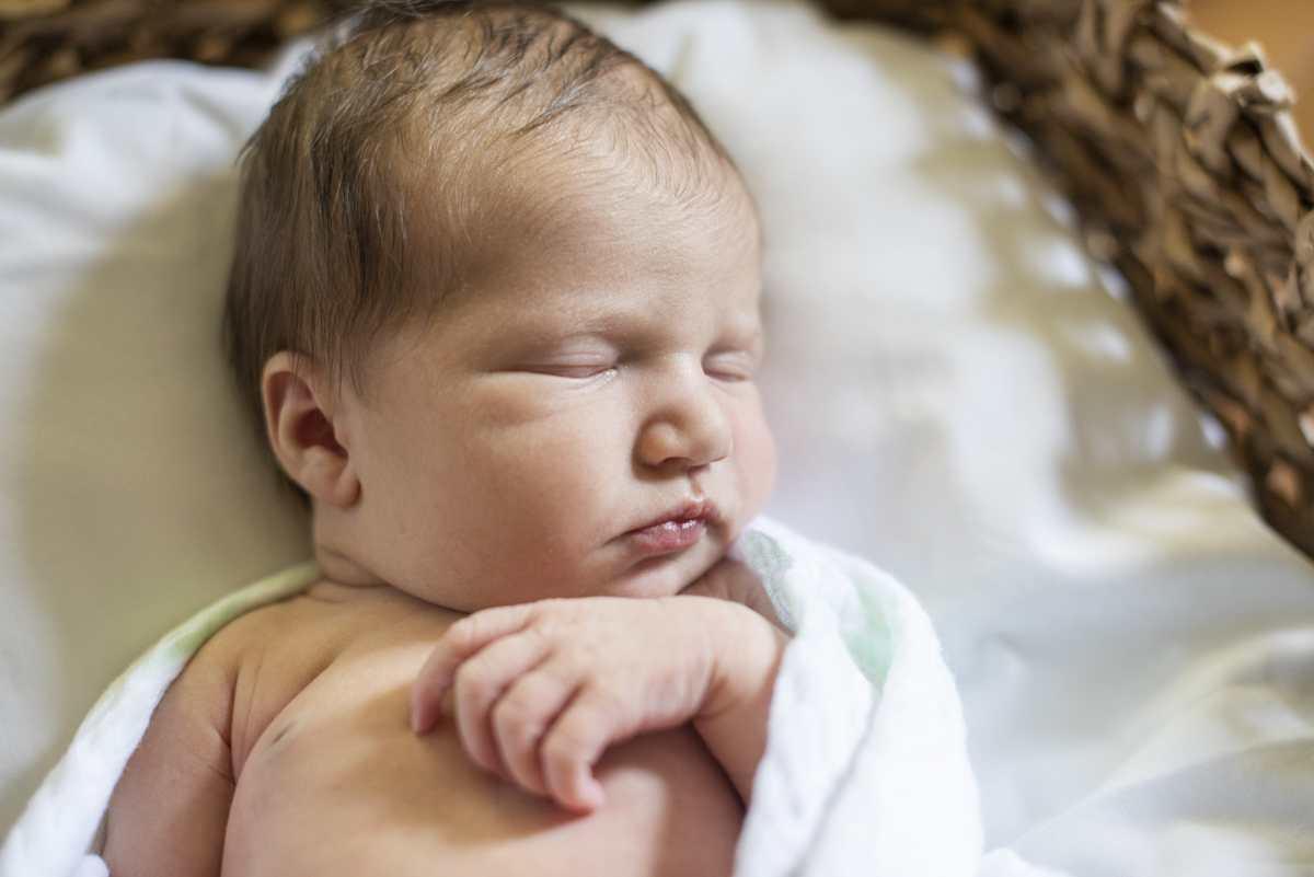 Newborn baby in white swaddle in basket