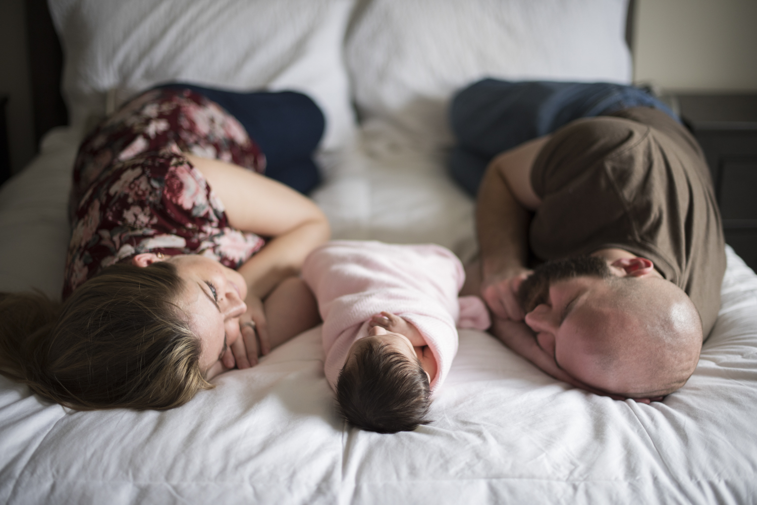 Parents looking at baby girl, all laying on bed during Newborn Photography in Asheville