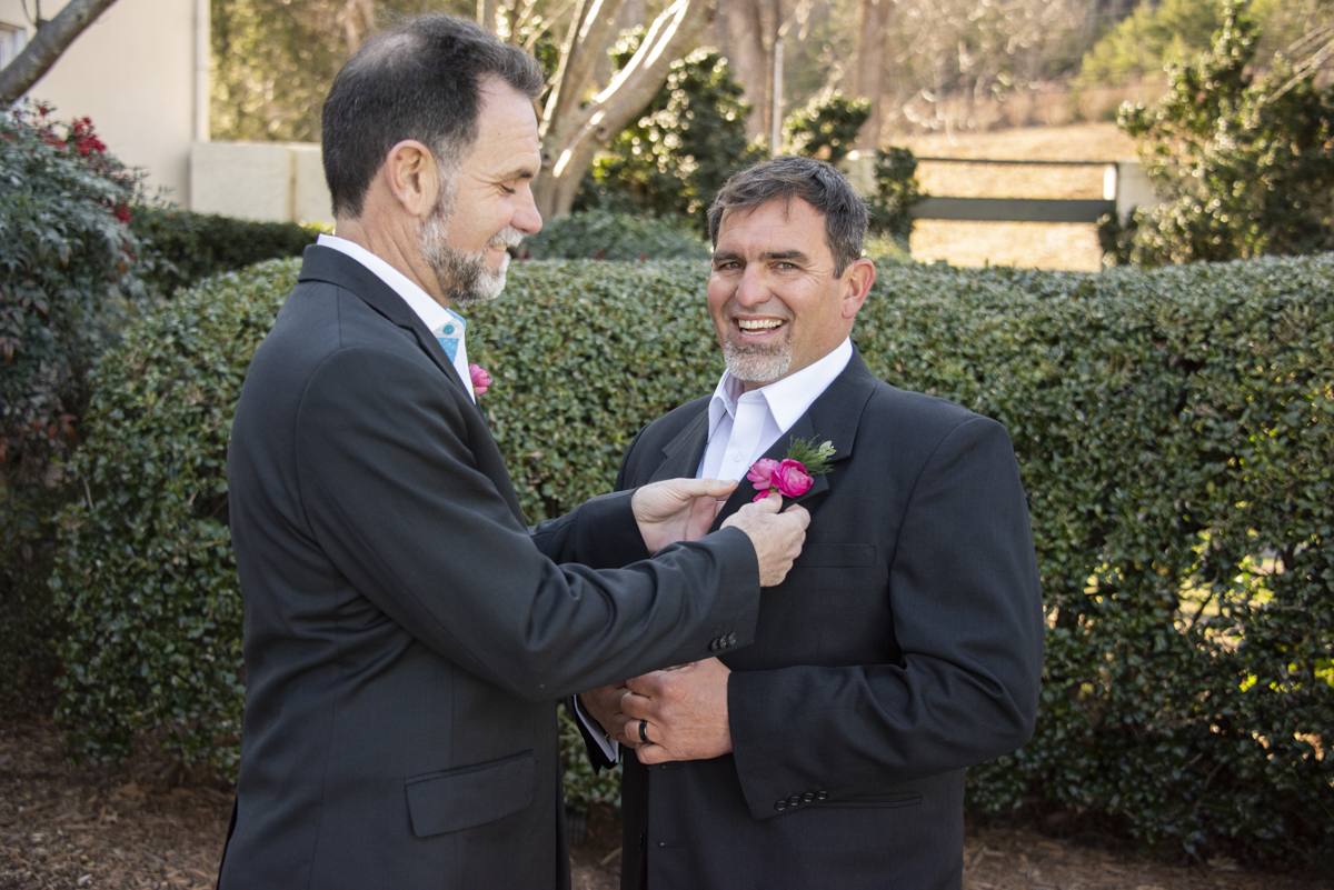 Groomsman pinning boutonniere to Groom during wedding