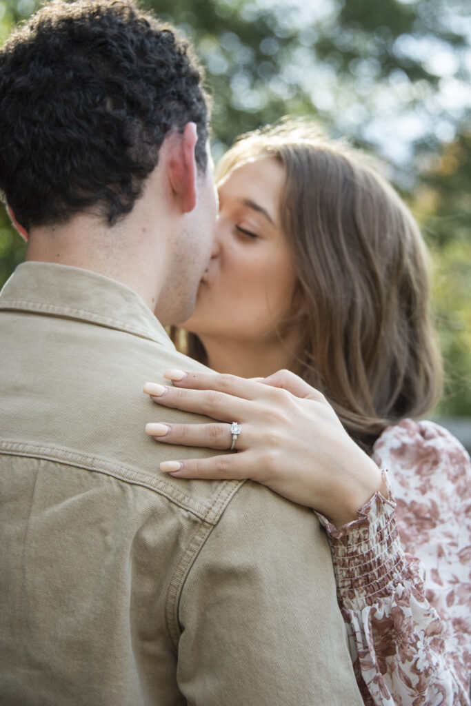 Couple kissing and showing engagement ring during fall photos in Asheville