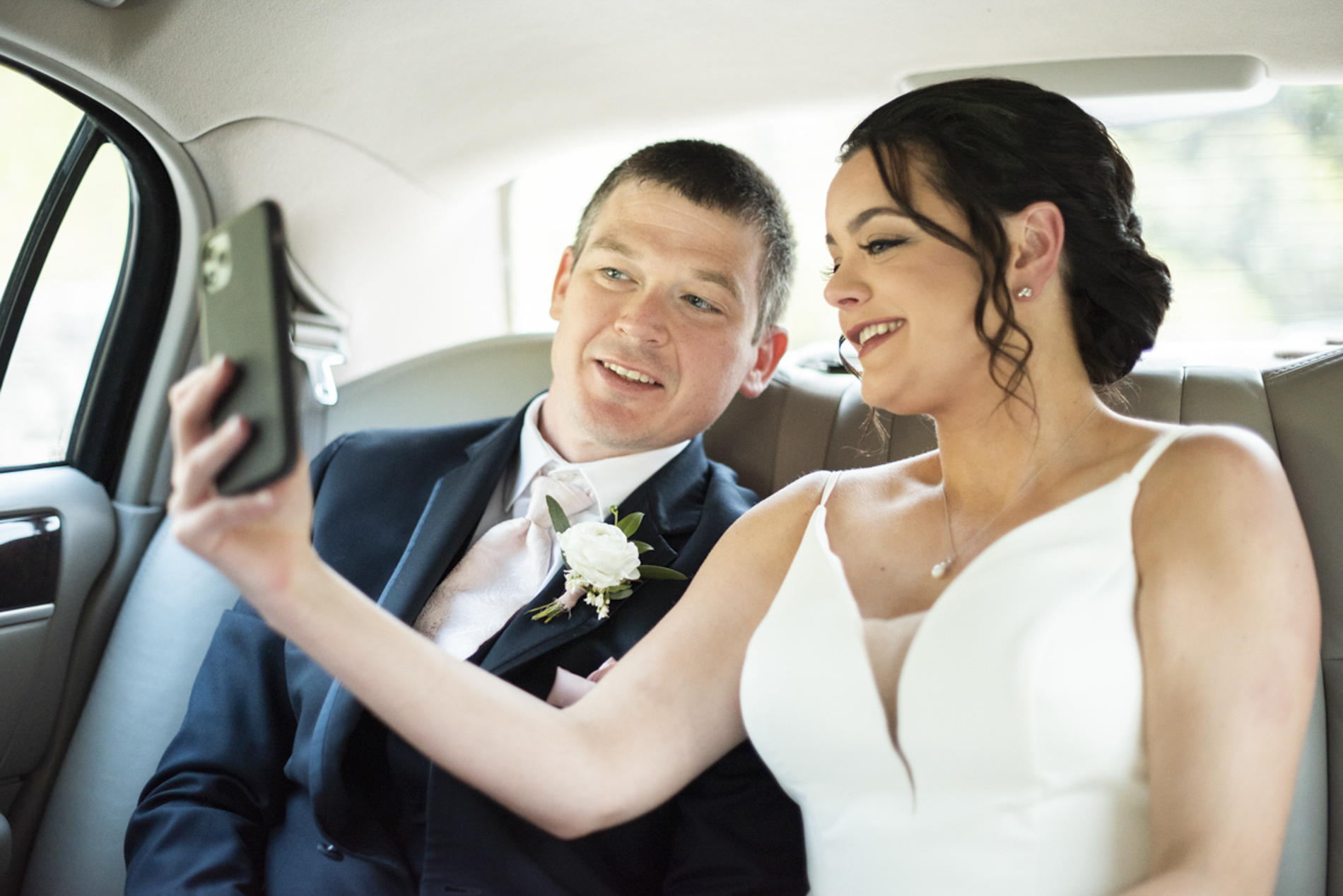 Bride and groom taking selfie in limo