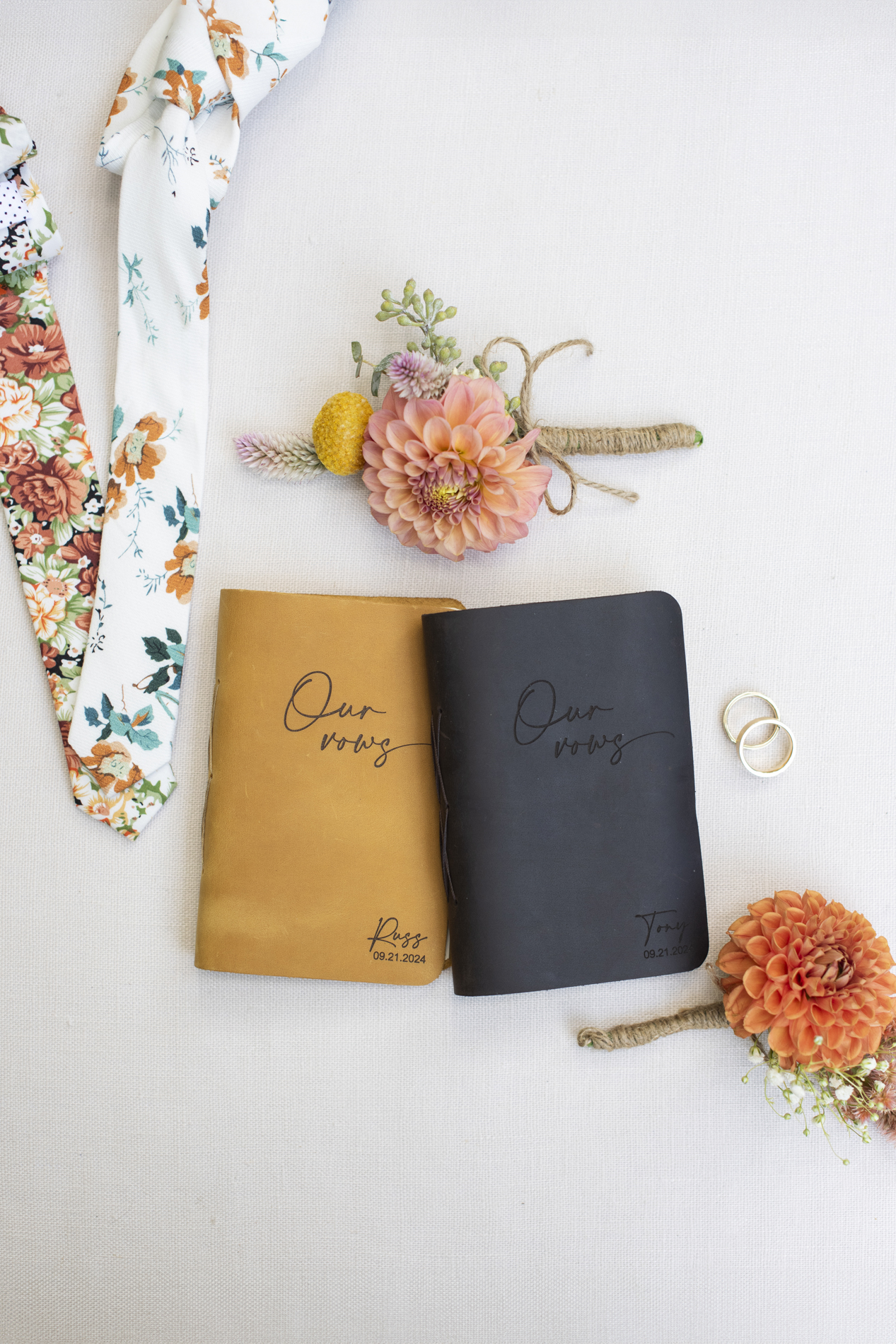 Details with vow books, flowers, ties at queer wedding