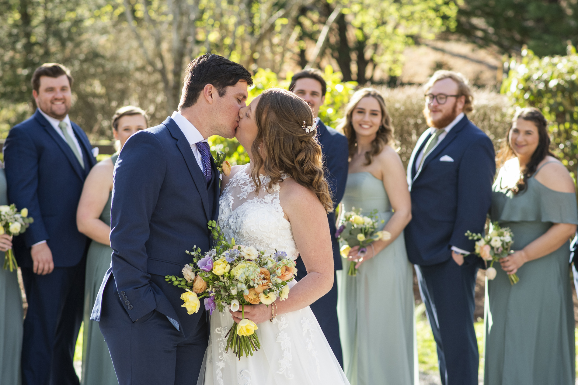 Couple kissing with wedding party behind