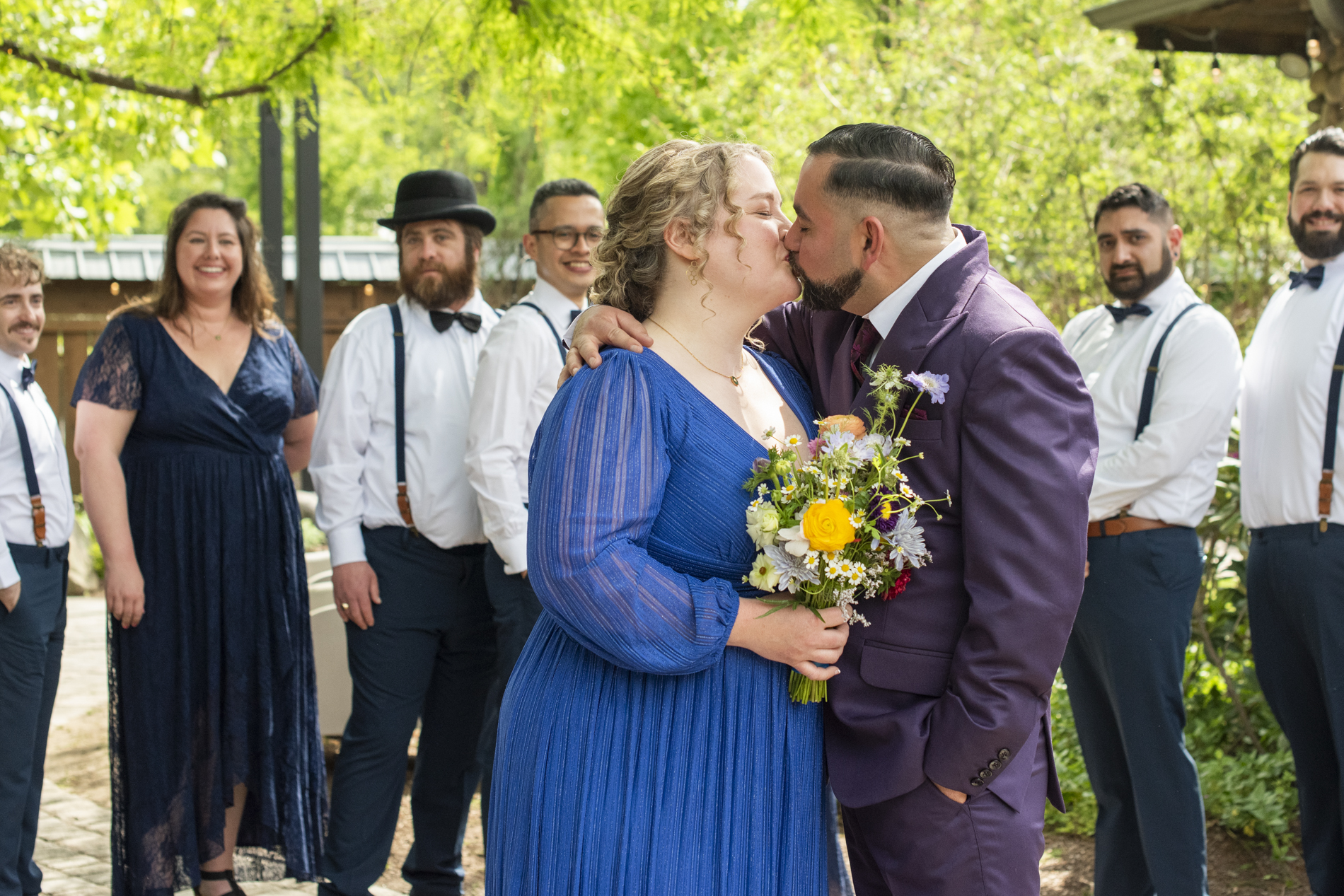 Bride and groom kissing with wedding party behind them
